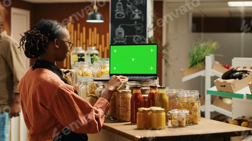 Preview: Woman merchant uses greenscreen on laptop and arranges products on stall