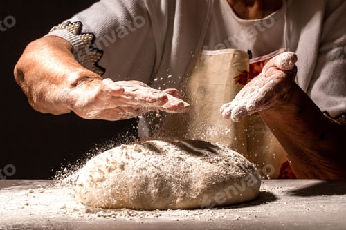 Preview: Woman great-grandmother clapping hands to dust a mound of freshly prepared pastry with flour