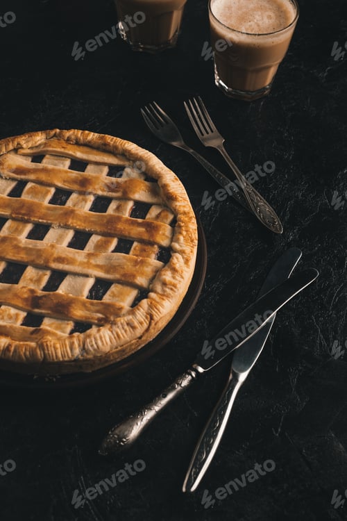 Preview: close up view of homemade berry pie, silverware and glasses of cacao isolated on black table