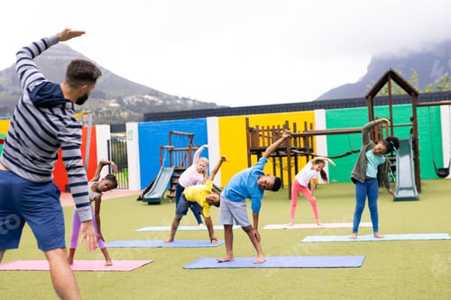 Preview: Diverse male teacher and elementary schoolchildren practicing yoga in schoolyard
