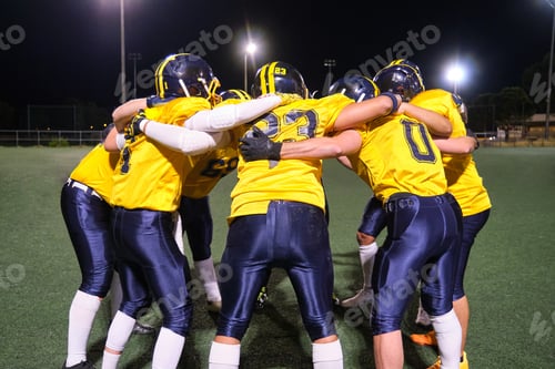 Preview: American football team huddling on field at night