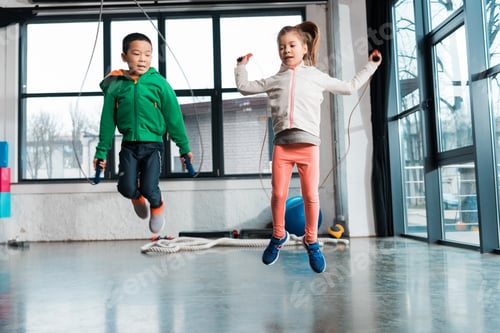 Preview: Front view of multicultural children doing exercise with jump rope in gym