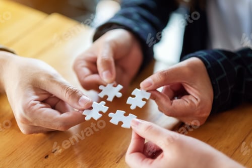 Preview: Closeup image of a group of people holding and putting a piece of white jigsaw puzzle together