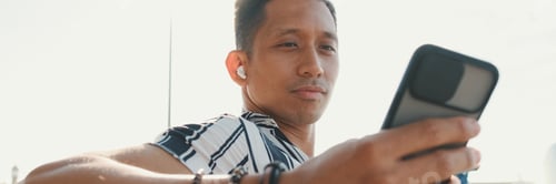Preview: Young man tourist sits on bench on the pier and uses mobile phone, panorama