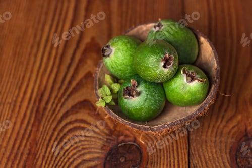 Preview: Green feijoa in a coconut shell hulf on a wooden background. Raw vegan food.Vitamin C. Copy space.