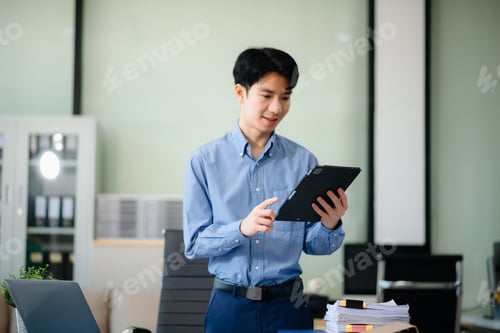 Preview: Confident Asian businessman typing laptop computer and digital tablet at office
