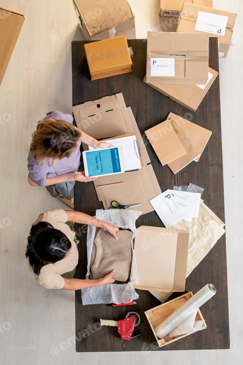 Preview: Young manager packing folded sweater while her colleague taking online payments