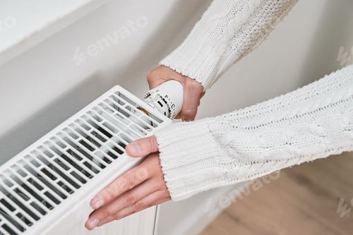 Preview: Woman in warm sweater adjusting temperature on heating radiator
