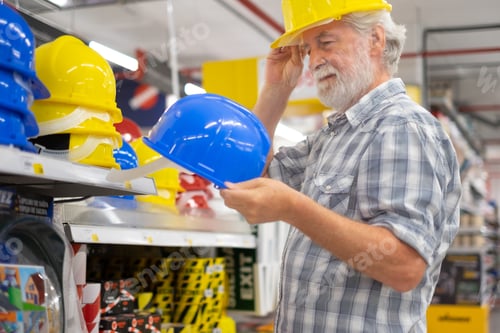 Preview: Senior bearded man in hardware store selects and tries a construction helmet