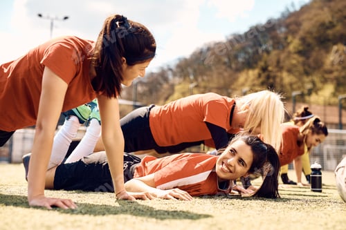 Preview: Happy female soccer team warming up for sports training on playing field.