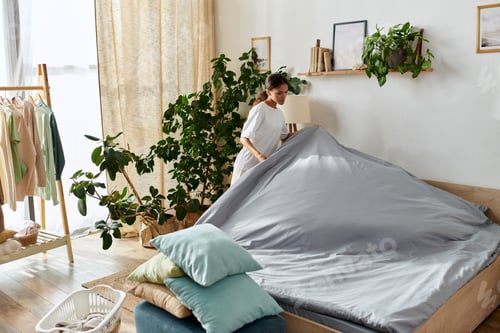 Preview: A young african american woman is making her bed while cleaning her stylish apartment.