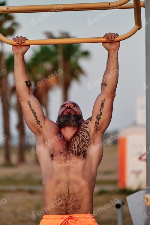 Preview: Strong sporty man doing pull-ups exercise during workout outdoors.
