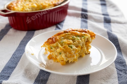 Preview: Tasty Homemade Cheddar Corn Pudding Casserole on a white plate, low angle view. Close-up.
