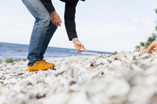 Preview: Low section of man picking stones at beach
