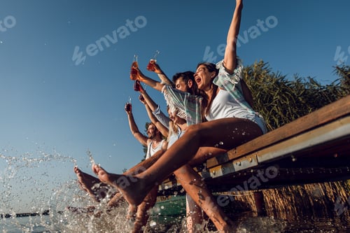 Preview: Group of friends sitting on the edge of a pier having fun and enjoying a summer day at the lake.