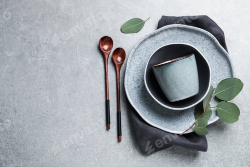 Preview: Set of dishware with eucalyptus leaves and napkin on grey table, flat lay. Space for text