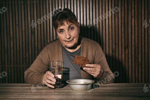 Preview: Poor senior woman with water and bread at table against wooden wall