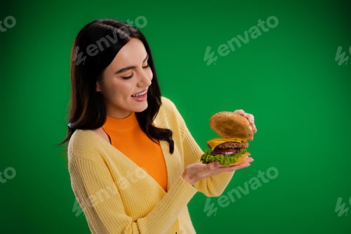 Preview: amazed woman looking at tasty burger with cheese and meat isolated on green