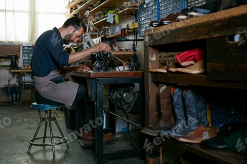 Preview: Male cobbler in traditional shoe workshop at sewing machine