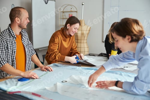 Preview: Cheerful couturiere laughing while cutting fabric material