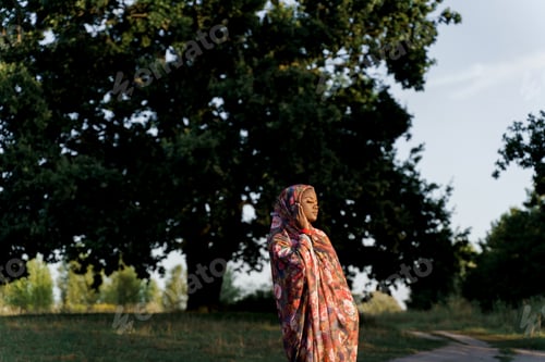 Preview: Black Muslim girl in traditional hijab touching scarf with closed eyes, serene moment