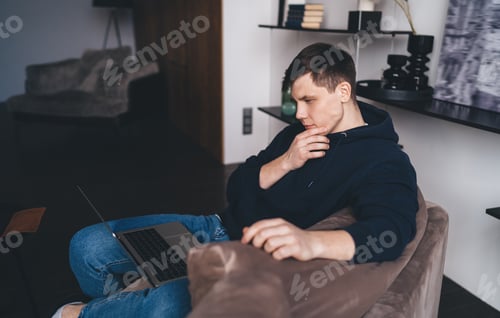 Preview: Pensive young man working on laptop in living room
