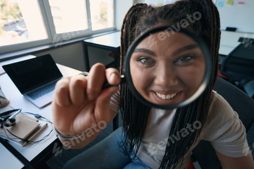 Preview: Joyous female office worker looking at something through loupe
