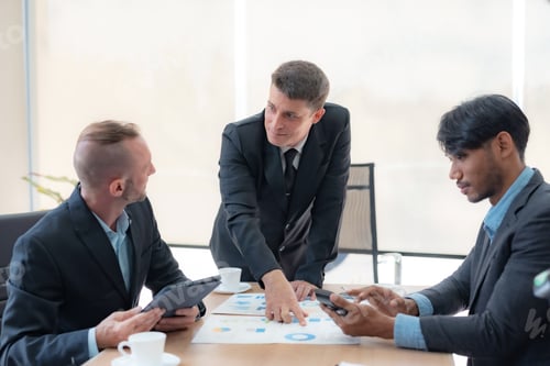 Preview: Group of diverse businessman going over paperwork together and working on laptop at meeting.