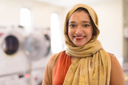 Preview: Face of happy young beautiful Indian Muslim businesswoman smiling as owner of the laundromat