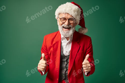 Preview: jolly Santa posing on green backdrop with thumbs up gesture and smiling sincerely, winter concept
