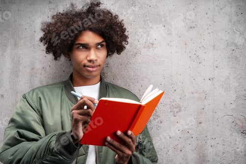Preview: Serious pensive curly African American man wearing green jacket holding orange notebook taking notes