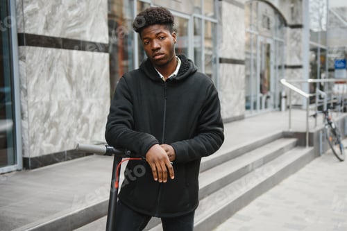Preview: Young african american guy with electric scooter in the city. The concept of ecological transport.