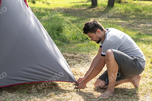 Preview: A man outdoors in the process of setting up a tent.