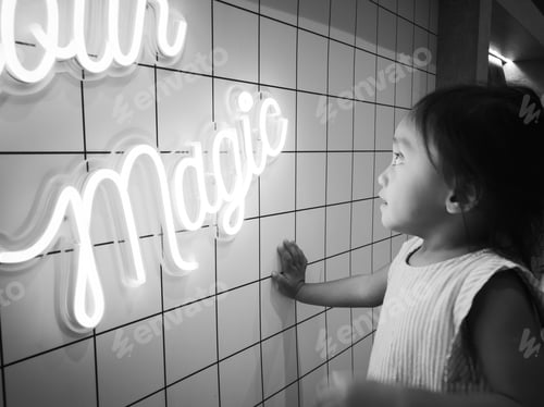 Preview: neon word MAGIC in black and white, toddler looking at it.