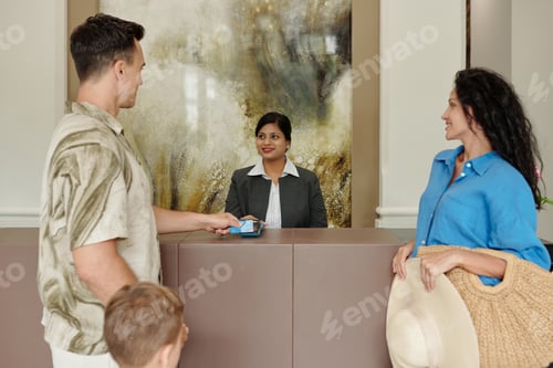 Preview: Family Checking into Hotel While Receptionist Smiling