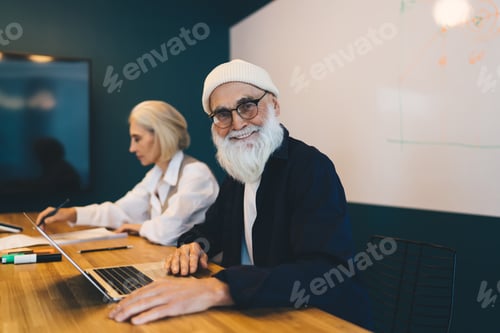 Preview: Smiling senior male and female employees sitting at table while working on project