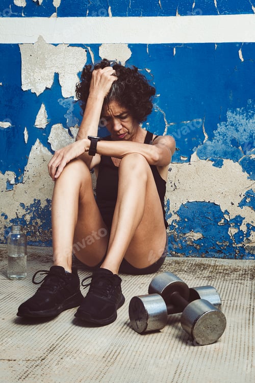 Preview: Adult woman sitting on the street frustrated after exercise