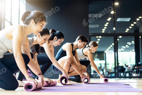 Preview: Group of sporty people rolling yoga mat after training yoga workout in studio room at gym fitness