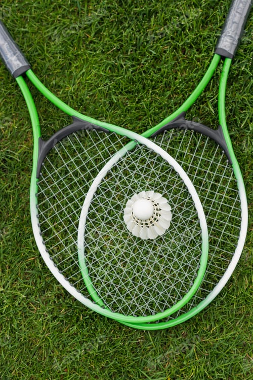 Preview: top view of shuttlecock on badminton rackets lying on green grass