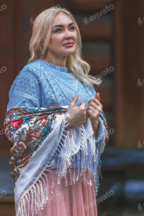 Preview: A blonde Russian woman in a national Russian headscarf on the porch of a log village house. Vintage