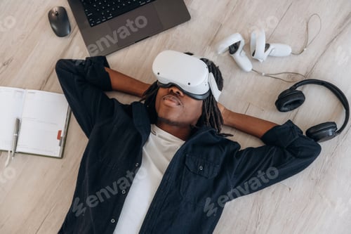 Preview: Laptop is nearby. Top view of man that is lying down on floor in virtual reality headset
