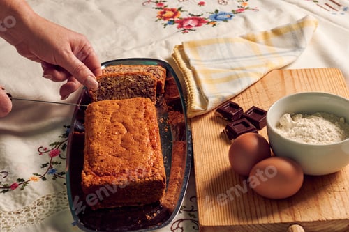 Preview: Hand of a woman with a knife cuts a sponge cake with some ingredients on a white tablecloth