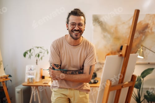 Preview: Portrait of smiling hipster artist with arms crossed standing at studio