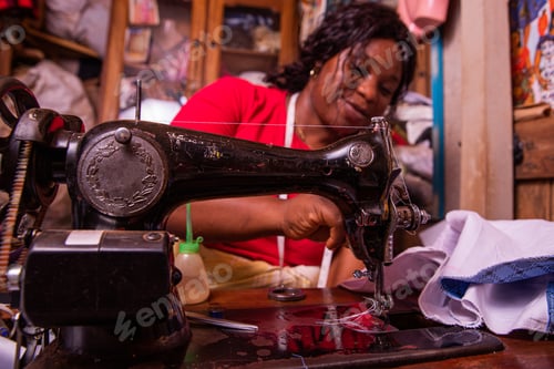 Preview: An African seamstress sews a dress with her sewing machine. Working female in her tailor shop