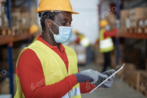 Preview: African man wearing safety face mask while working inside industrial warehouse