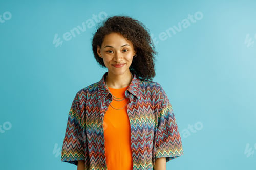Preview: Portrait of charming smiling woman looks camera while standing on blue studio background