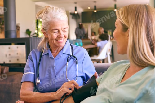 Preview: Senior Midwife Visiting Pregnant Woman At Home Taking Blood Pressure With Family In Background