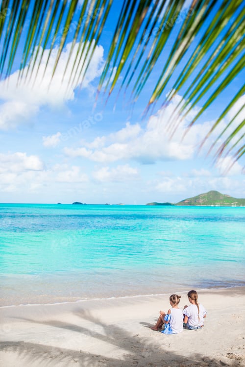 Preview: Back view of little girls on sandy beach. Happy kids sitting under the palm tree on tropical beach