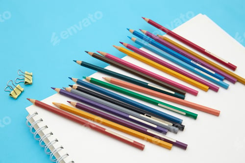 Preview: Top view of many colorful pencils and paper clips on a blank notebook