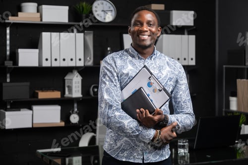 Preview: portrait of young black businessman with financial documents in his hands standing near table in